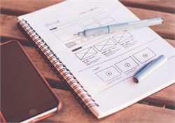 Hand-drawn interface wireframes sketched in a notebook beside a pen and phone